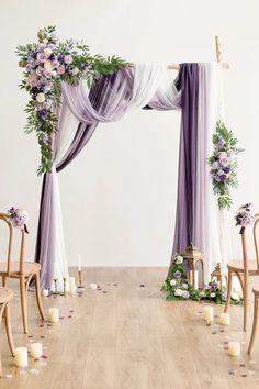 an arch decorated with purple and white flowers, candles and greenery for a wedding ceremony