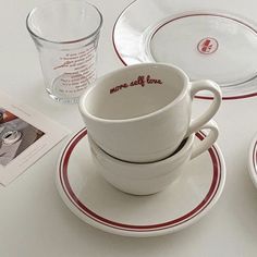 there is a cup and saucer on the table next to two plates with red trimmings