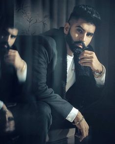 a man with a beard sitting in front of a mirror wearing a suit and tie