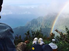 two people sitting on top of a mountain with a rainbow in the background