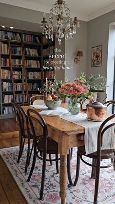 a dining room table with chairs and a chandelier hanging from the ceiling in front of bookshelves