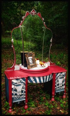 a red vanity with a mirror on it in the grass next to some plants and trees