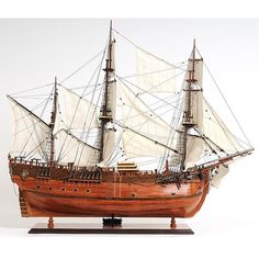 a wooden model ship with white sails on a black base and brown wood trimmings