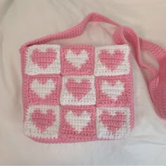 a pink and white crocheted bag with hearts on it sitting on a bed