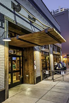 the outside of a restaurant with people sitting at tables under an awning over the entrance