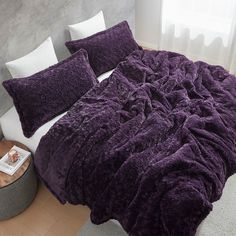 a bed with purple comforter and pillows on it