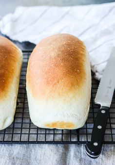 two loaves of bread sitting on top of a cooling rack next to a knife