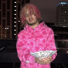 a man with pink hair and money in his hands is wearing a pink camouflage print hoodie