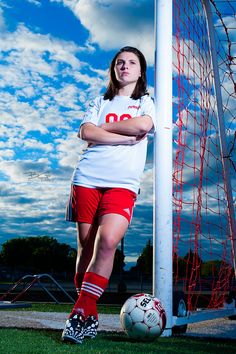 a girl in red shorts and white shirt standing next to a soccer goal with her arms crossed