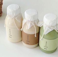 three jars are lined up next to each other on a white surface with a basket in the background