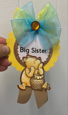 a hand holding up a big sister ornament with a blue bow on it