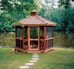 a wooden gazebo sitting on top of a lush green field next to a river