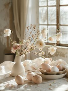 an arrangement of flowers and eggs in a vase on a table with white linens