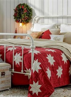 a white metal bed with red and white bedspread on top of it next to a christmas wreath