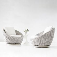 two white chairs and a vase with a plant in it sitting on a white floor