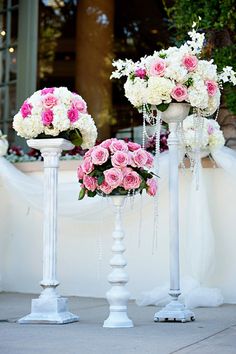 three white and pink flower arrangements on pedestals in front of a wedding ceremony venue