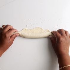 two hands are kneading dough on a white surface, while another hand is holding something in the other hand