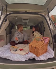 two women sitting in the back of a van with picnic blankets and baskets on it