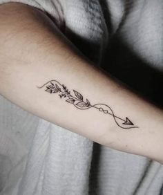 a woman's arm with an arrow and flowers tattoo on the left side of her arm