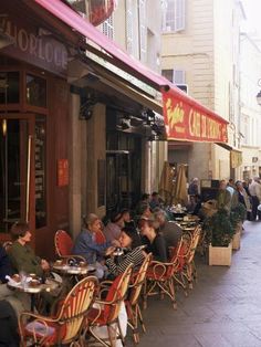 people sitting at tables in front of a restaurant on the sidewalk outside with red awnings