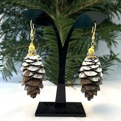 * The Top Halves Of The Pinecones Are Frosted To Resemble Snow, And Have A Light Varathane Coating For Preservation. The Gold Settings Are A Glass Gold Round Ball Bead Atop A Gold-Plated Rondelle Bead With Clear Rhinestones. The Fishhook Earwires Are Gold-Plated. Add A Touch Of Nature To Your Look With These Handmade Dangle Drop Earrings. Made From Real Natural Pine Cones, Each Earring Is Unique In Shape And Size. The Cone-Shaped Earrings Are Set In Gold-Plated Metal With A Hook Closure For Easy Pine Needle Earrings, Pine Cone Earrings, Pine Cone Scale Earrings, Nature-inspired Drop Earrings With Natural Inclusions, Nature-inspired Brown Pendant Jewelry, Gold Color Combination, Boutique Jewelry, Clear Rhinestones, Brown Gold