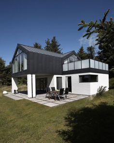 a modern house in the middle of a grassy area with tables and chairs on it