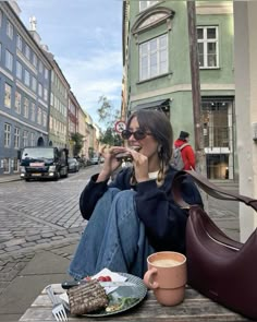 a woman sitting on a bench eating food and drinking coffee