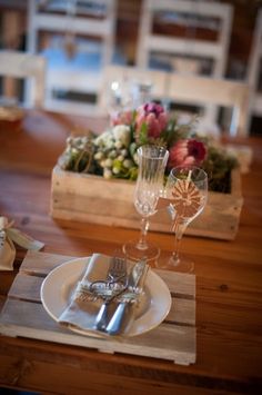 the table is set with silverware and flowers in a wooden box on top of it