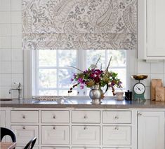 a vase with flowers sitting on top of a kitchen counter next to an open window