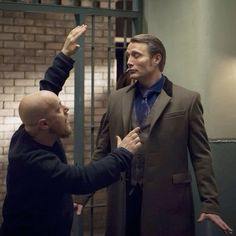 two men standing next to each other in front of a brick wall and metal bars