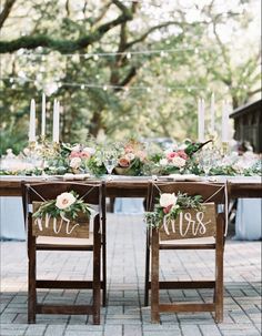 a wooden table topped with chairs covered in flowers and greenery next to a sign that says mr and mrs rustic wedding chair signs