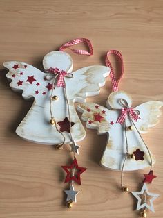 two wooden angel ornaments with red and white stars hanging from them on a wood surface