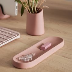 a pink computer keyboard sitting on top of a wooden desk next to a vase filled with flowers