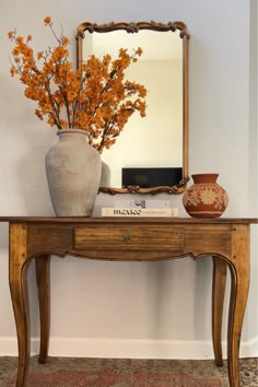 a vase with flowers sitting on top of a wooden table next to a large mirror