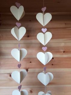 paper hearts hanging from strings on a wooden wall