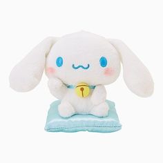 a white stuffed animal sitting on top of a blue pillow with a yellow bell in it's mouth