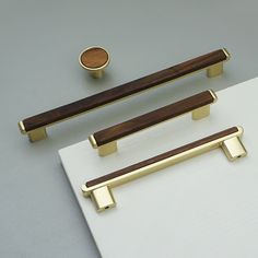 two brass handles and one wooden handle on a white surface