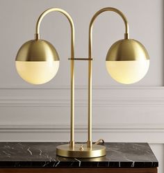 two brass lamps on a marble table with white walls in the background and gold accents