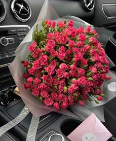 a bouquet of pink roses sitting on top of a car dashboard next to a steering wheel