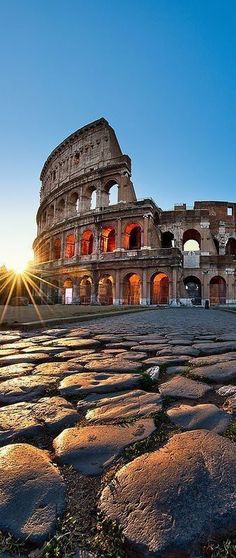 the sun is setting over an old roman colossion in rome, italy with cobblestones on the ground