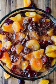 a glass bowl filled with fruit on top of a wooden table next to sliced oranges and cranberries