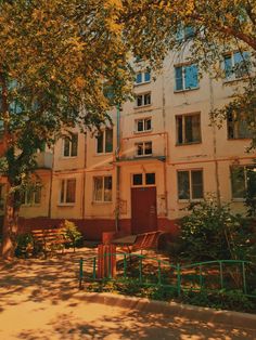 an apartment building with trees in front of it and benches on the sidewalk near by