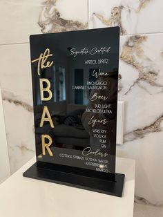 a black and gold bar sign sitting on top of a white countertop next to a marble wall