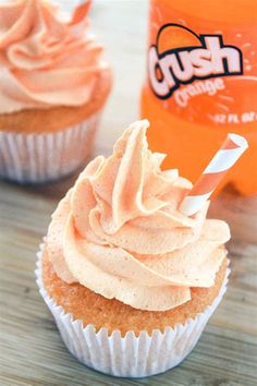 two cupcakes with frosting and an orange soda bottle in the back ground