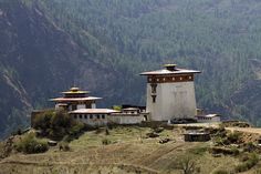 an old building sitting on top of a hill with mountains in the background and trees around it