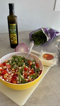 a yellow bowl filled with salad sitting on top of a counter next to a bottle of olive oil