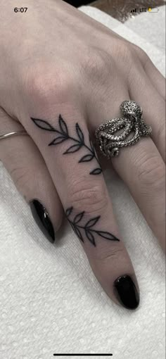 a woman's hand with black nail polish and tattoos on her fingers, holding a ring