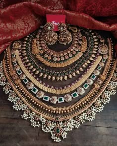 an elaborate necklace and earring set is displayed on a wooden floor in front of a red curtain