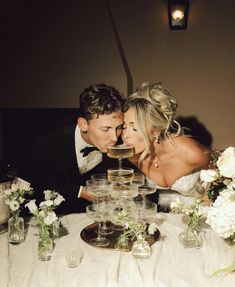 a bride and groom kissing in front of wine glasses on a table with white flowers