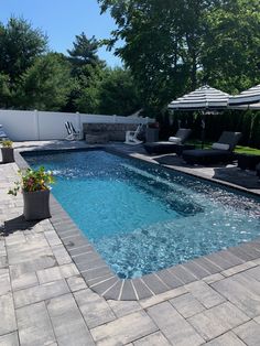 an empty swimming pool with lounge chairs and umbrellas in the back yard, surrounded by greenery